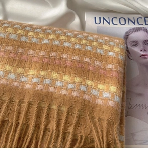 Close-up of caramel plaid scarf with thick fringe tassels on elegant white fabric