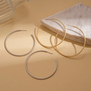 Matte textured gold and silver C-shaped hoop earrings on elegant marble display