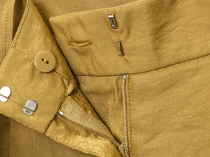 Detail of ginger yellow metallic fabric waistband with buttons and zip closure