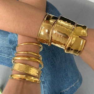Detail of stacked gold hammer-textured bangles and a wide-surface minimalist cuff