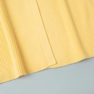 Gros plan sur la texture du tissu en maille côtelée jaune citron et les finitions soignées