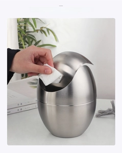 Close-up of a hand opening the swing lid of a silver egg-shaped stainless steel desk bin