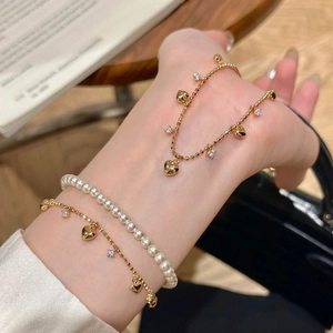 Dettaglio di eleganti braccialetti dorati a strati con ciondolo a cuore e perle al polso