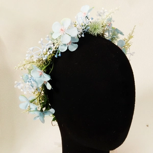 Detail view of a floral headband with blue and white artificial flowers on a black model
