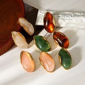 Detail view of four pebble-shaped resin earrings with gold-plated frames in autumn tones