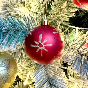 Close-up of red matte Christmas ball with silver glitter snowflakes on snowy tree branch