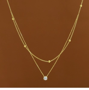 Detail of a double-layered 18K gold-plated necklace with gold beads and a zircon pendant