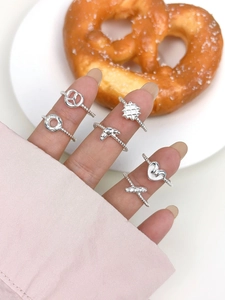 Close-up of heart-shaped and knotted s925 silver rings on fingers near pretzel