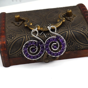 Macro detail of handmade silver wire wrapped spiral earrings with purple amethyst beads