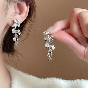 Detail of silver floral tassel earrings with leaf-shaped metal pendants worn by a model