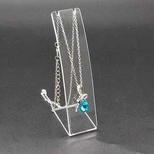 Close-up of a blue water drop crystal necklace hanging on an acrylic display stand