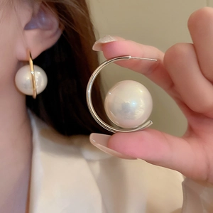 Close-up of elegant C-shaped pearl earring shown on model and held in hand for detail
