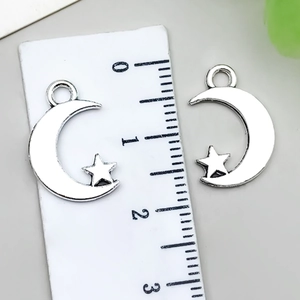 Close-up of antique silver moon and star charms showing 2cm size on a measuring ruler