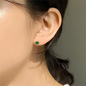 Close-up of minimalist sterling silver heart stud earrings featuring green zircon on ear