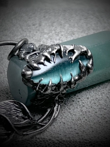 Close-up of gothic silver claw pendant holding an oval turquoise gemstone with leaf details