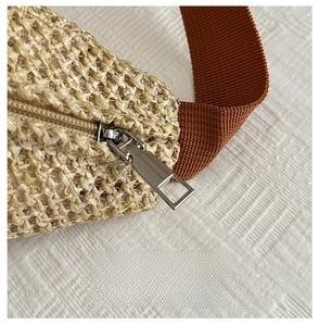 Detail of woven straw texture with silver metal zipper and brown fabric strap