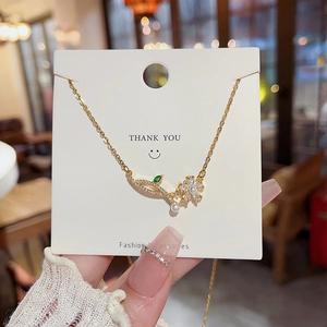 Detailed close-up of a golden flower petal necklace with a pearl on a display card