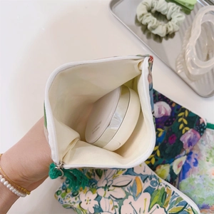 Macro view of floral cotton pouch showing zipper with green tassel and interior storage