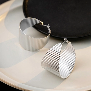 Detailed view of silver C-shape metal earrings with textured vertical striped finish