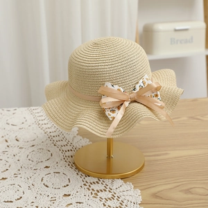 Détail d'un chapeau de paille avec ruban champagne et nœud floral sur présentoir doré
