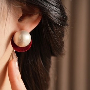 Detail view of pearl earrings with red velvet backing worn on model's earlobe