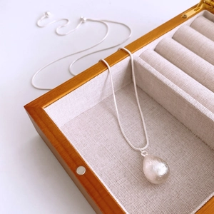 Gros plan du pendentif goutte argenté brossé sur chaîne serpent dans un coffret bijoux