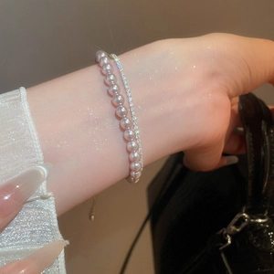 Close-up of layered light pink pearl and single row rhinestone bracelets set for women