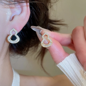 Close-up of golden hollow gourd earrings with zircon inlay worn by a model