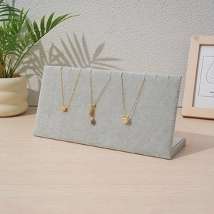 Gray velvet jewelry display stand for gold necklaces on a wooden table with green plant