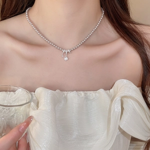 Gros plan du collier de perles avec pendentif nœud en cristal et breloque cœur
