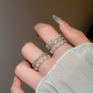 Detailed close-up of multilayered gold ring set with pearls and rhinestones on fingers