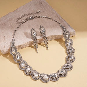Detailed view of silver teardrop rhinestone necklace and matching tassel earrings on stone