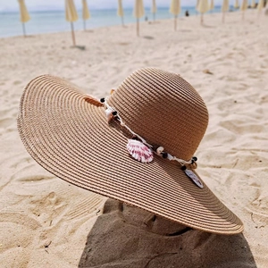 Detail of wide brim straw sun hat with shell decoration and beads on beach sand
