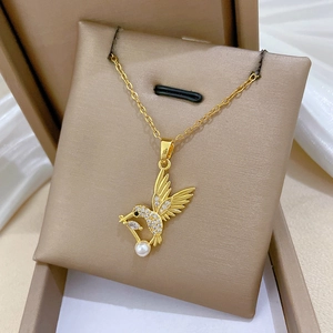 Gros plan d'un collier colibri doré avec perle blanche dans un écrin cadeau de luxe