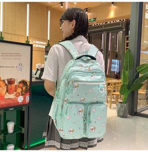 Mint green school backpack with white cartoon bear prints worn in a cafe setting