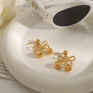 Elegante goldene Kirsch-Ohrstecker mit Schleife aus Edelstahl auf weißem Keramiktablett