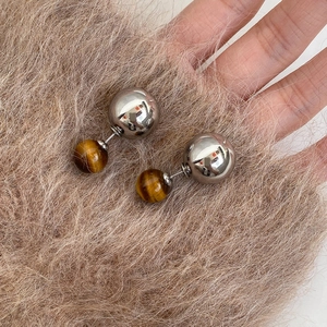 Detailed view of silver stud earrings with brown tiger eye stone beads on plush fabric
