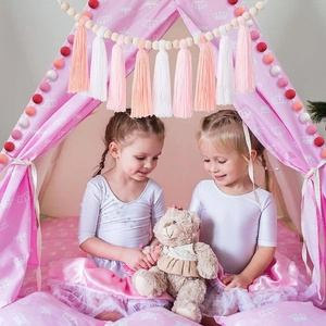 Cozy pink kids tent with pompom tassels and girls playing inside with a teddy bear