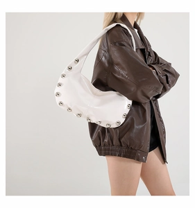 Close-up of a white patent leather crescent bag with silver studs on a shoulder