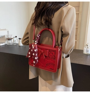 Detail of red bridal handbag with floral embroidery, decorative bow, and silk scarf handle