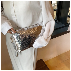 Detail of sequined mini clutch bag with silver wrist strap held by a fashion model