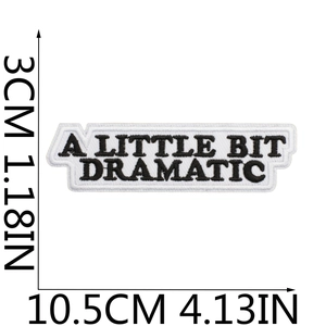 Detail of embroidered patch showing A LITTLE BIT DRAMATIC text in black on white background