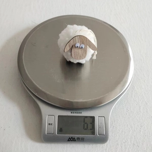 Close-up of handmade white wool felt sheep ornament on a digital scale weighing 6.3 grams