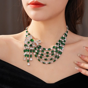 Gros plan détaillé d'un collier nœud en argent avec pierre émeraude et chaînes à pompons