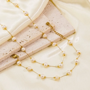 Elegant gold titanium necklace with white pearls on silk champagne fabric backdrop