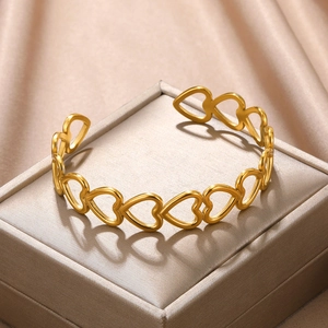 Close-up of golden hollow heart pattern open bangle on elegant champagne silk fabric