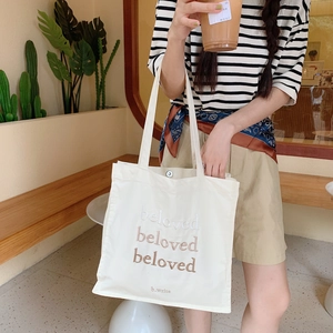 Gros plan du sac fourre-tout en toile beige avec broderie beloved et bouton pression