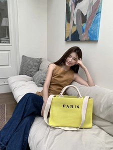 Detail of a bright yellow straw tote bag with PARIS print shown in a lifestyle setting