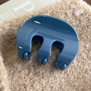 Macro shot of smooth blue acrylic M-shaped hair claw clip with glossy finish and minimalist design