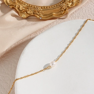 Dettaglio di una collana a catena dorata ad onde d'acqua con singola perla d'acqua dolce